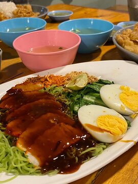 Jade noodles with roasted pork and boiled egg on a white plate.