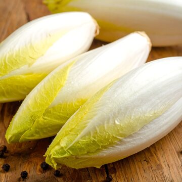 Three endives with light green & white leaves on wood with black peppercorns