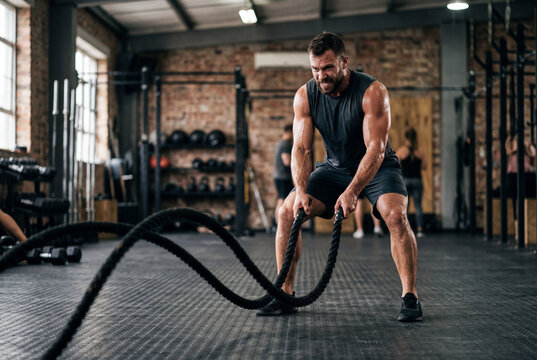 Hombre atl&eacute;tico entrenando con cuerdas de batalla en gimnasio industrial
