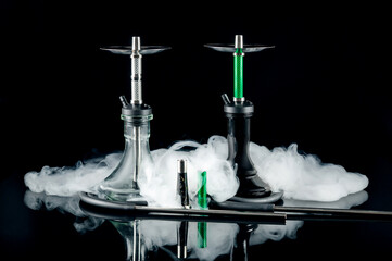 Two hookahs with white puffs of smoke on a black mirror background. Artistic shooting in a studio.