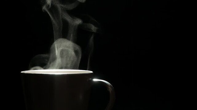 Mug of Hot Coffee. A trickle of steam rises and twists gracefully from a cup of hot Coffee. Backlight illuminates brown cup on a black background