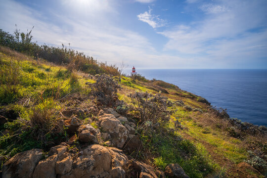 Panoramic view of dramatic cliffs and rugged coastline at Ponta do Pargo, Madeira island, Portugal. Famous view of a lighthouse on a rock surrounded by the blue and wild Atlantic Ocean.