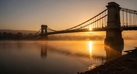 Fototapeta premium Suspension bridge at sunrise over calm water with mist