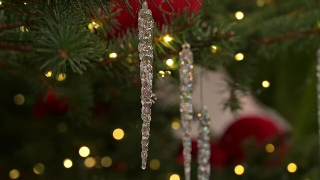 Close up of glass icicle Christmas tree ornaments hanging on evergreen branches with warm bokeh lights