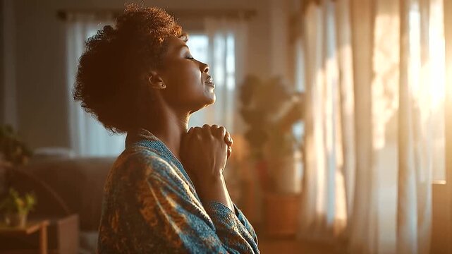 Faceless African woman from behind in a bright home interior kneeling beside a window with hands clasped in prayer soft morning light streaming through sheer curtains and