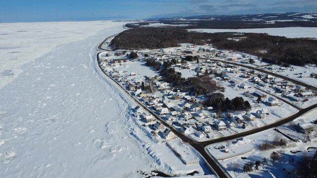 Aerial footage of Saint-Ulric-de-Matane in Gaspe Peninsula. Discover a picturesque snow-covered coastal village bordered by the frozen Saint Lawrence River.