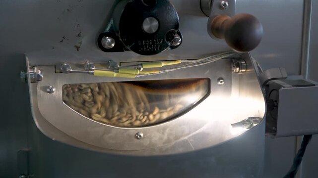 Industrial coffee beans tumbling inside a roasting drum window, transforming raw green beans into aromatic brown roast coffee - 4K stock video