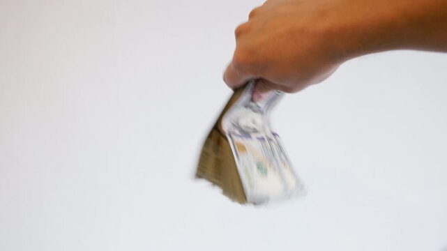Adult person energetically fans a stack of paper currency in a bright indoor setting. Motion blur adds dynamic feel to the abstract financial scene.