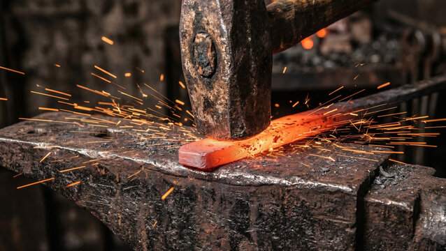 Close-up of a heavy hammer striking glowing red hot steel on an anvil with bright orange sparks
