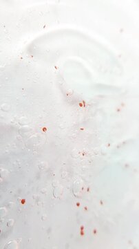 Spreading and mixing clear gel serum containing red pigment or stains using a metal applicator. Cosmetic texture art, skincare product visualization, abstract beauty concept.