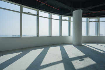 Obraz premium Empty modern office space with floor-to-ceiling windows casting geometric shadows on concrete floor and white column