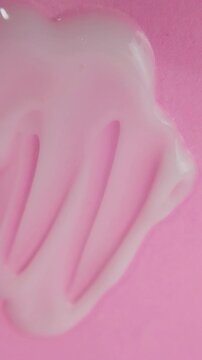 Spreading and expanding white serum evenly across a pink surface using a metal applicator tool. Smooth texture application, skincare concept