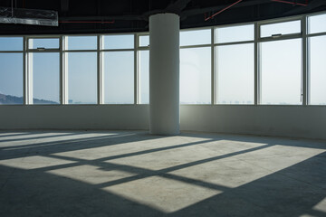 Obraz premium Empty modern office space with floor-to-ceiling windows casting geometric shadows from a central column