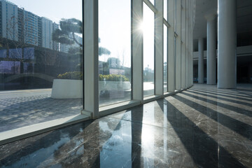 Obraz premium Sunlight streams through floor-to-ceiling windows into a modern building interior with marble flooring and architectural columns