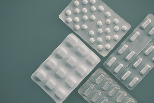 Tablets and capsules in pharmaceutical packaging arranged on a minimal grey-green background