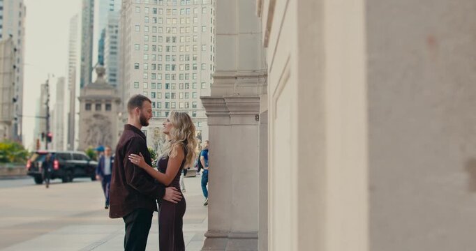 A beautiful loving couple stands on a street in a big city, frozen in a gaze into each others eyes while people and cars move around them. A special romantic moment. Downtown.