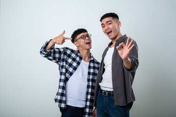 Fototapeta premium Two Asian men pose happily with playful expressions. One points at the other, while the other makes an 