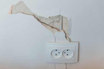 Damaged White Wall With Cracked Plaster Above Double European Electrical Outlet Showing Exposed...