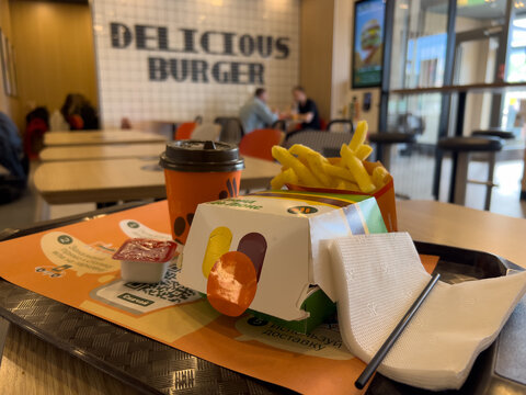 Moscow, Russia - 1 September 2025: Fast food meal with french fries, a drink, and a burger box on a table in a blurred modern restaurant interior