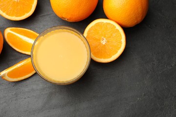 Citrus juice in glass and fresh oranges on black table, flat lay. Space for text