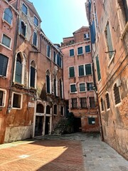 Obraz premium Historic buildings in Venice with faded pink walls and green shutters. Narrow street with pavement and historical architecture create the atmosphere of an old European city.