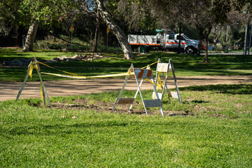 Obraz premium Caution tape and barriers block off a section of a grassy park with trees and a truck in the background