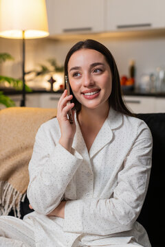 Young woman at night home enjoys smartphone call smiles listens speaks in friendly tone. Caucasian girl on sofa at evening talks with friend shares news gossip happy chat voice enjoys communication.