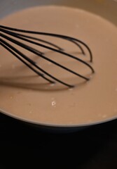 Fototapeta premium Close-up of pancake batter being mixed with a whisk in bowl. Conceptual food image representing homemade cooking, traditional dessert preparation and family kitchen concepts.