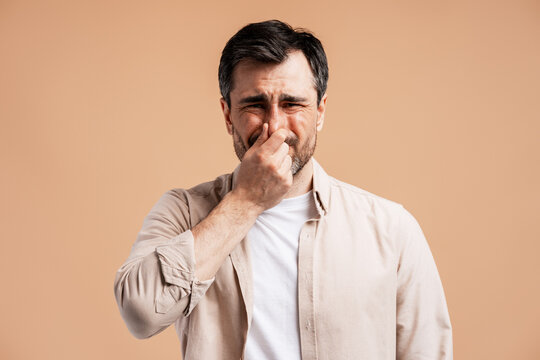 Man pinching nose, reacting to bad smell, feeling disgust and unpleasant odor