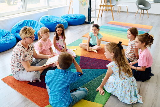 Teacher reading a story to children during circle time in a colorful preschool classroom
