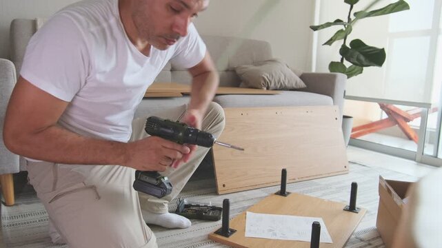 Man installing legs on new flat-pack furniture using a power drill at home