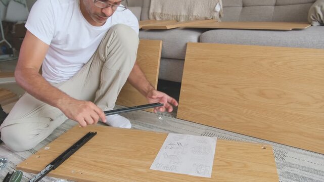 Man carefully assembles new wooden furniture on the floor following the paper instructions
