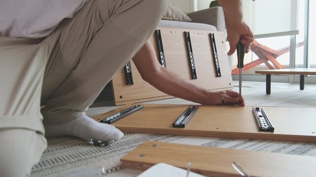 Man putting together new flat-pack furniture at home, tightening a screw with a screwdriver