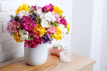 Beautiful freesia flowers in vase and candles on wooden table near white brick wall indoors, closeup. Space for text © New Africa
