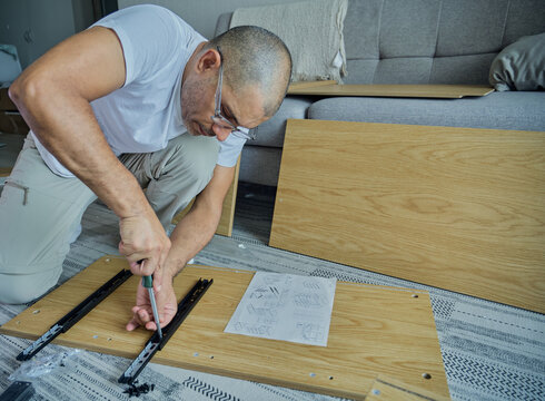 Man assembling furniture parts at home, creating new desk and storage solutions