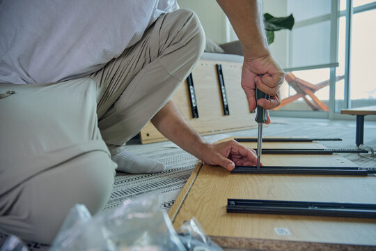 Man building new wooden furniture using a screwdriver and tools on the floor