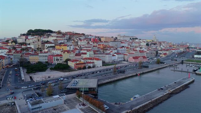 Cinematic aerial panorama of Lisbon old town with dense historic buildings, red rooftops and the Tagus river creating a classic European coastal city landscape