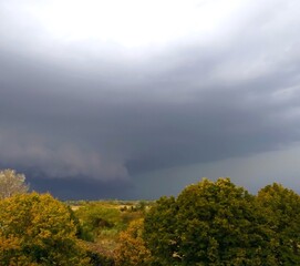 Large thundercloud, a gloomy storm cloud over a field of trees. Panoramic view of a rural landscape. Cloudy weather, partly cloudy. The natural beauty of nature's colors.