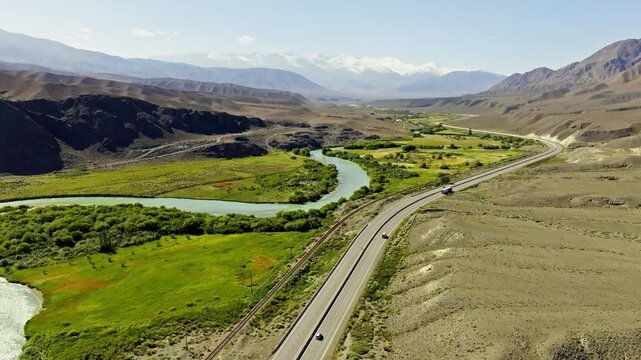 Aerial view captures expansive rural landscape in Kyrgyzstan, showcasing mountains, valleys, and a winding Chu river. Peaceful daytime scene highlights natural beauty.