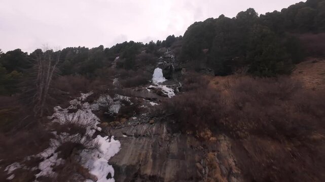 Aerial Shot of a Waterfall Cascading Through a Dense ine Forest on a Mountain Sope