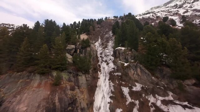 Cinematic Aerial Shot of a Stream Flowing Down a Stee Rocky Slope with Pine Tres