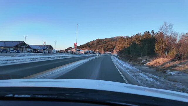 Dashboard camera view from a white car driving through  a rural winter landscape in Straumsnes, near Kristiansund, Norway.