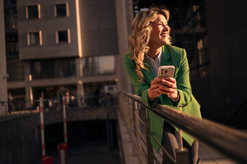 Happy business woman using smartphone in city at golden hour © Jelena