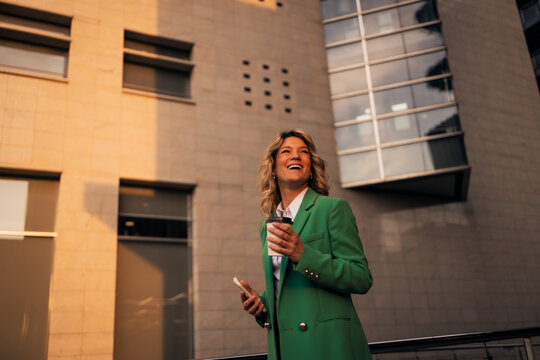 Business woman smiling, drinking coffee, using phone in city