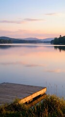 Fototapeta premium Serene lake at sunset with wooden dock and mountain silhouettes reflecting in calm water creating peaceful evening atmosphere for relaxation and nature themes.