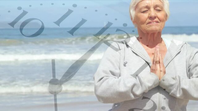 Senior woman on shore holding prayer hands breathing making clock spin camera rising meditating sea