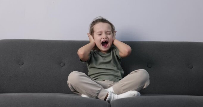 Autism. Little girl with sensory issues screaming on sofa indoors