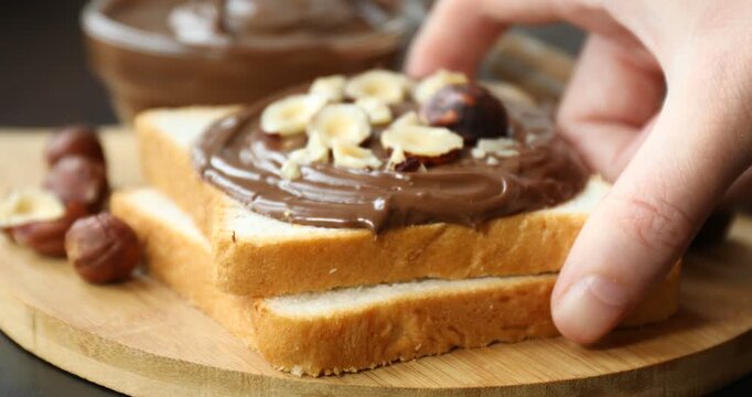 Woman putting toast with chocolate paste and hazelnuts onto table, closeup