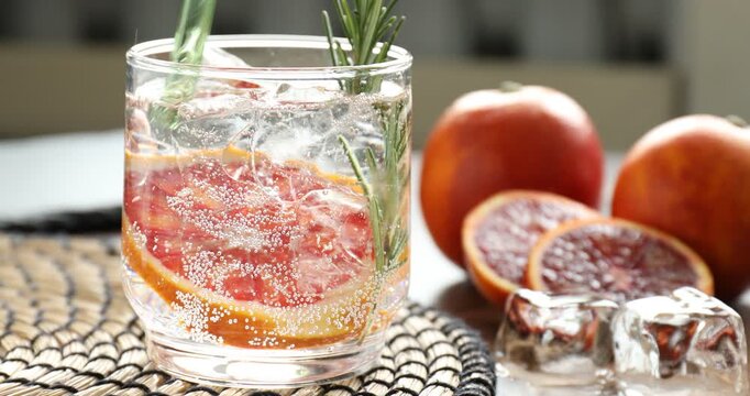 Stirring refreshing drink with Sicilian orange in glass at table, closeup
