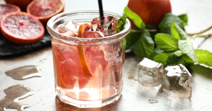 Stirring refreshing drink with Sicilian orange in glass at table, closeup